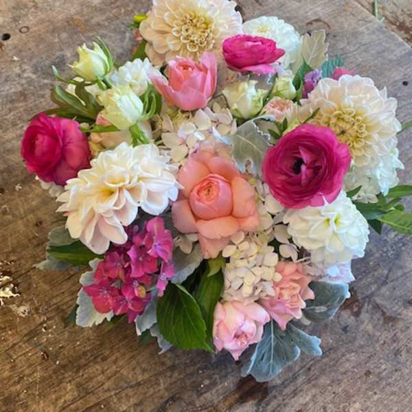 Round bouquet of pink, white, and peach flowers on a wooden surface