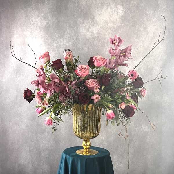 Large pink and burgundy floral arrangement in a gold urn vase