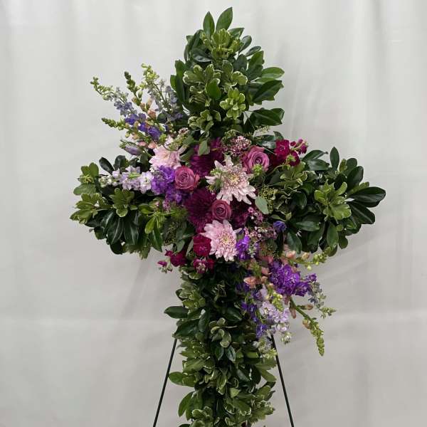 Large cross-shaped floral tribute with purple and pink flowers on a stand