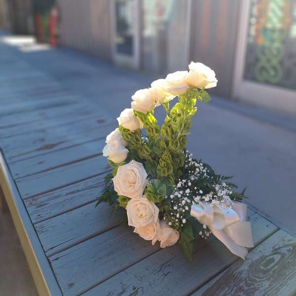 White roses and green snapdragons arranged with baby's breath and a satin ribbon