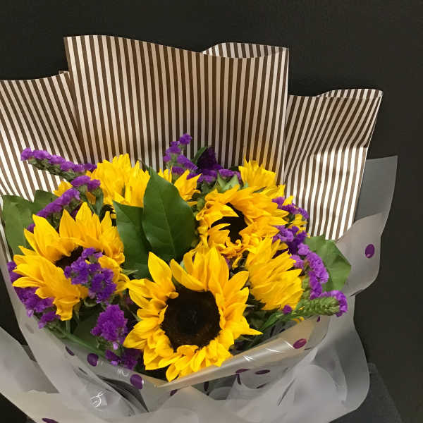 Bouquet of yellow sunflowers with purple filler flowers in striped wrap