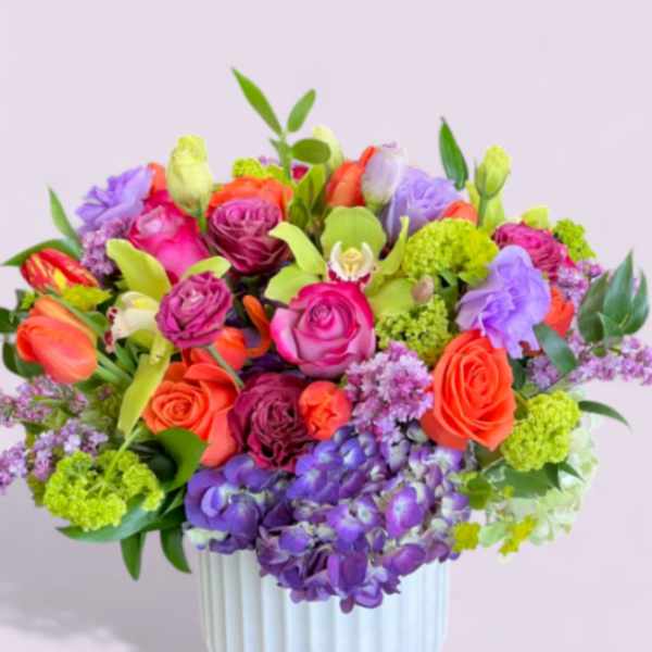 Bright mixed arrangement of orange, pink, and purple flowers in a white ceramic vase