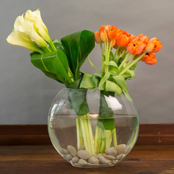 White calla lilies and orange tulips in a round glass vase