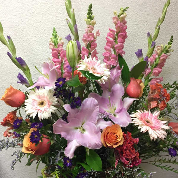 Mixed bouquet with pink lilies, roses, and tall snapdragons in a basket