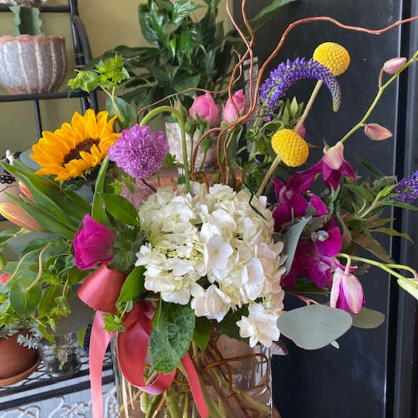 Mixed bouquet with hydrangea, sunflower, orchids, and pink tulips in a glass vase