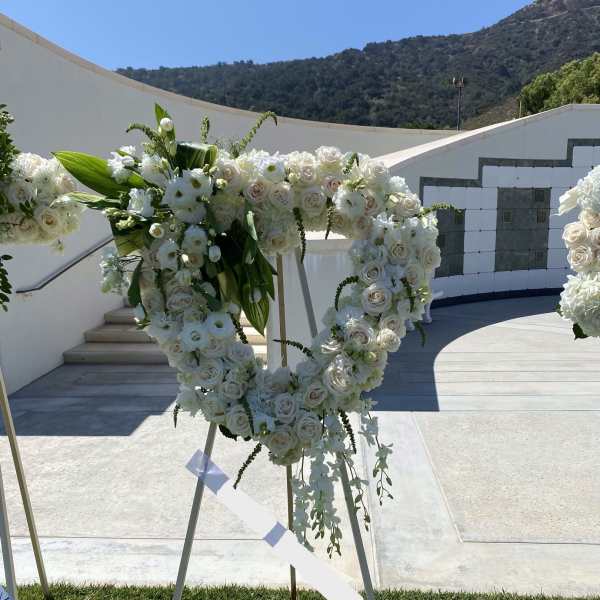 Heart-shaped white rose standing wreath with cascading white blooms on an easel outdoors