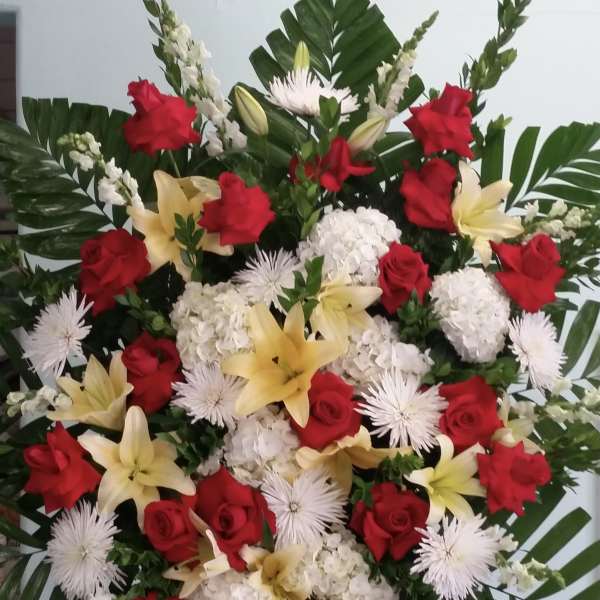 Large standing floral spray with red roses, white blooms, and yellow lilies
