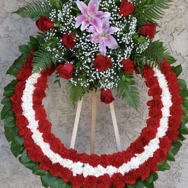 Standing floral wreath with red roses, pink lilies, and red-and-white garlands