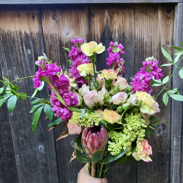 Handheld bouquet with pink and yellow flowers and a large protea