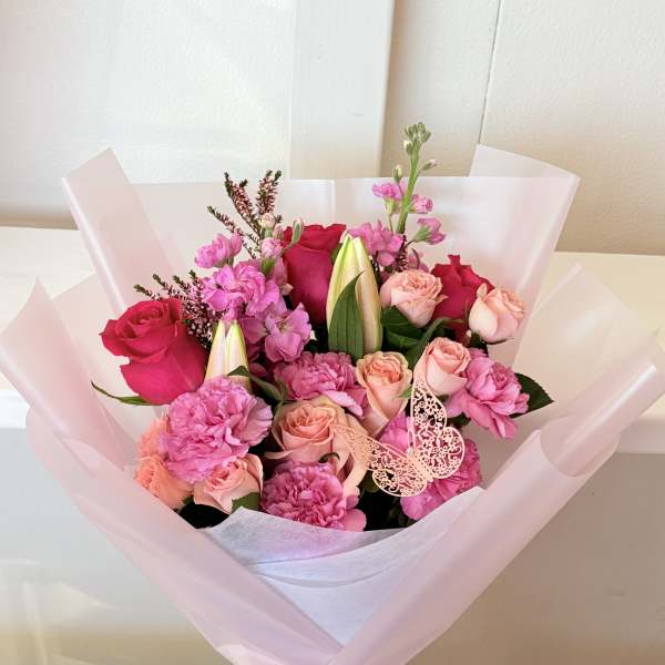 Pink and peach rose bouquet with carnations and lilies in pale pink wrap