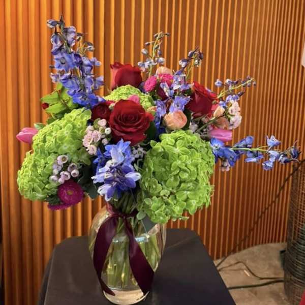 Bouquet of red roses, green hydrangeas, and blue flowers in a glass vase