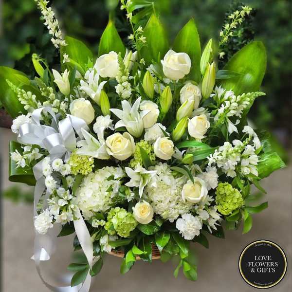 Large white and green sympathy basket with roses, lilies, hydrangeas, and a white ribbon bow.