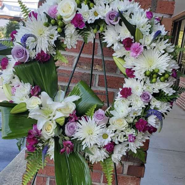 Large floral wreath with white, lavender, and pink flowers on a stand