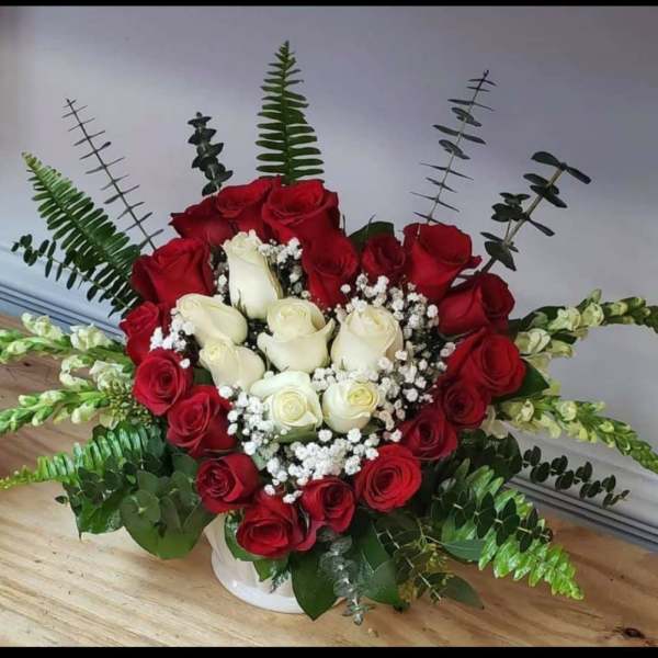 Red and white roses arranged in a white vase with baby's breath
