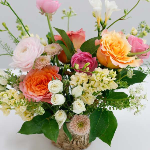 Mixed bouquet of roses, ranunculus, and white blooms in a rustic container