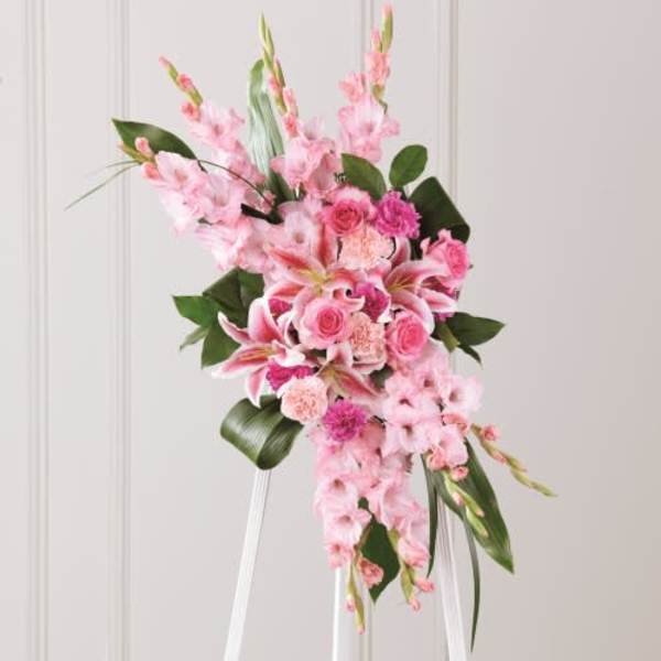Pink floral standing arrangement with lilies and roses on a white easel