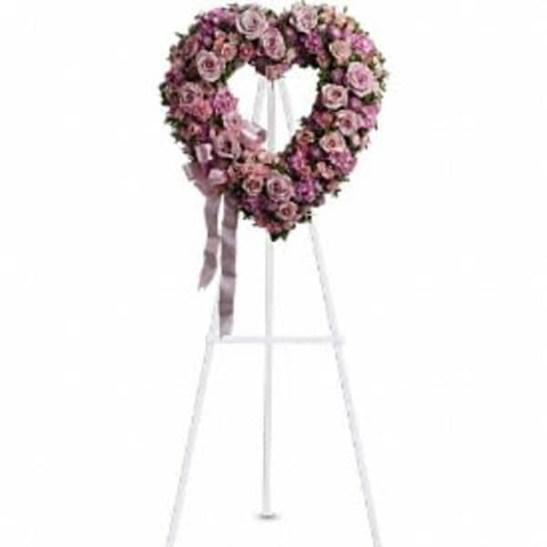 Heart-shaped pink floral wreath on a white stand with ribbon