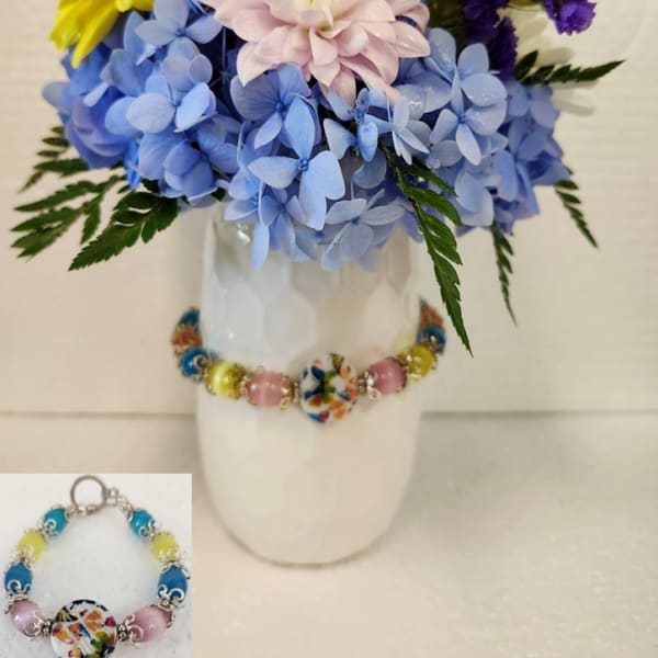 Colorful bouquet in a white vase with blue, yellow, purple, and pale pink flowers.