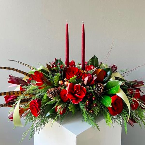 Red floral centerpiece with two tall candles and pinecones