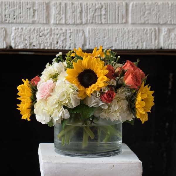 Sunflowers, roses, and white hydrangeas in a clear glass vase