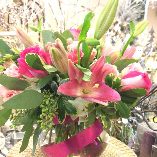 Pink lilies and roses arranged in a glass vase with a magenta ribbon