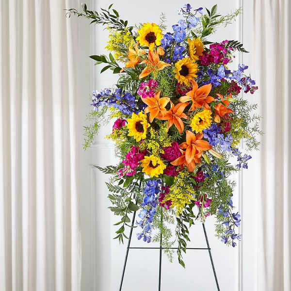 Tall standing floral spray with sunflowers, lilies, and blue flowers