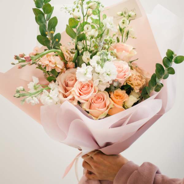 Handheld bouquet of peach and white roses with airy white blooms