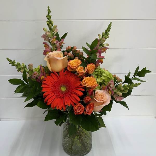 Mixed bouquet with orange gerbera daisies and peach roses in a glass vase