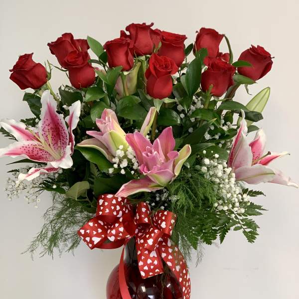 Bouquet of red roses and pink lilies in a red glass vase with a heart ribbon