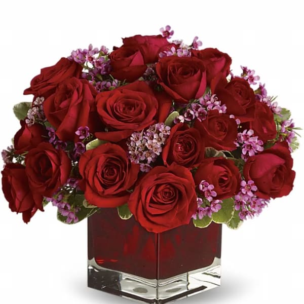 Red roses and small purple flowers in a square glass vase