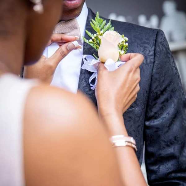 Person pinning a white rose boutonniere onto a man's suit jacket