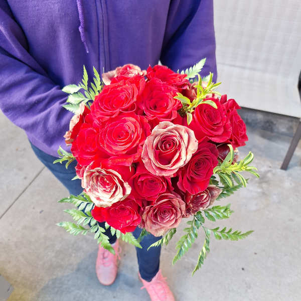 Handheld bouquet of red and blush roses with fern accents
