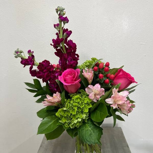 Bouquet of pink roses, green hydrangea, and purple blooms in a glass vase