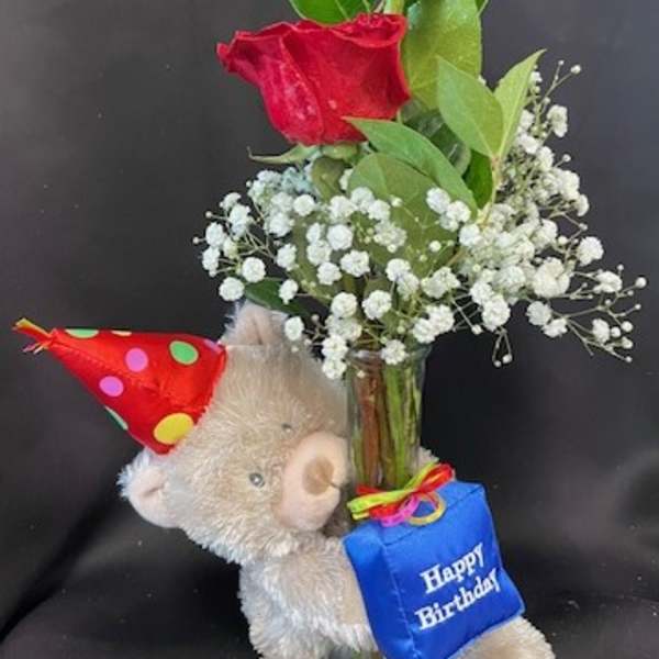 Red roses in a glass vase with a teddy bear and birthday tag