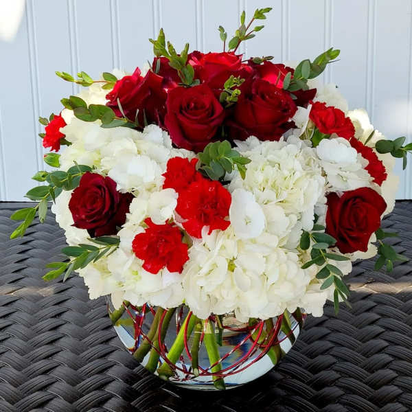 Red roses and white hydrangeas in a glass vase with greenery