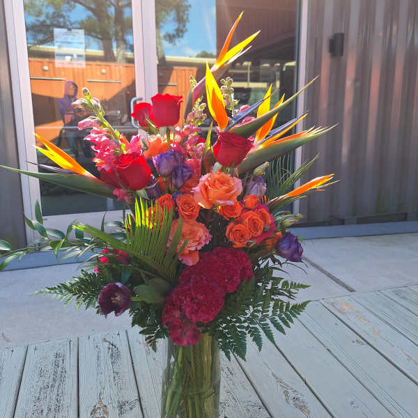 Tall tropical bouquet with red and orange roses in a glass vase