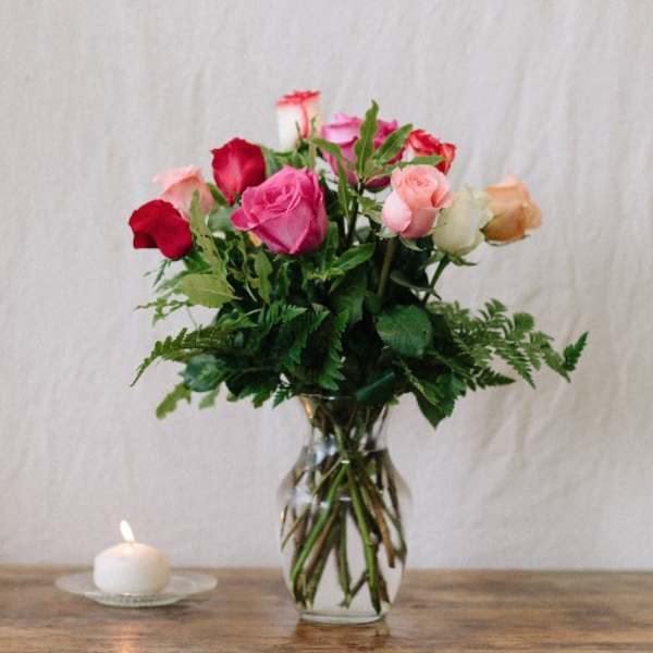 Mixed roses in a clear glass vase beside a small candle.