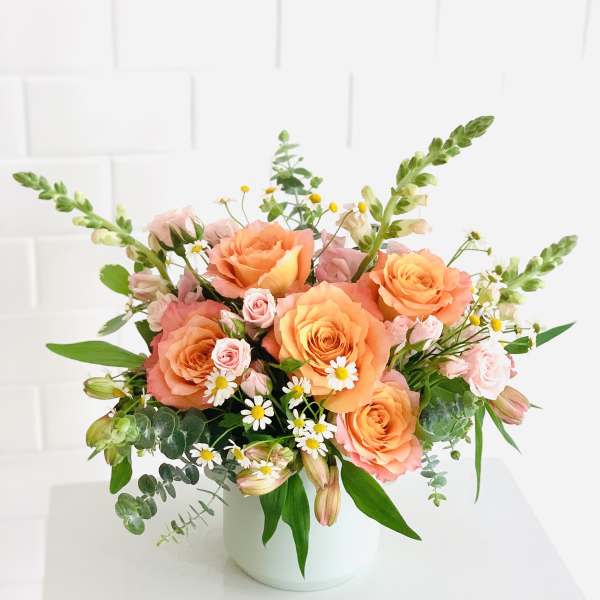 Peach roses and pink spray roses in a white vase