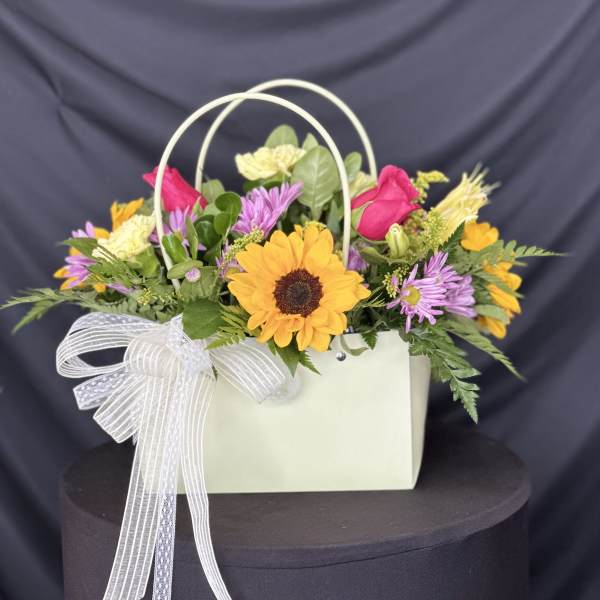 Mixed flower arrangement in a white handled gift bag with a ribbon bow