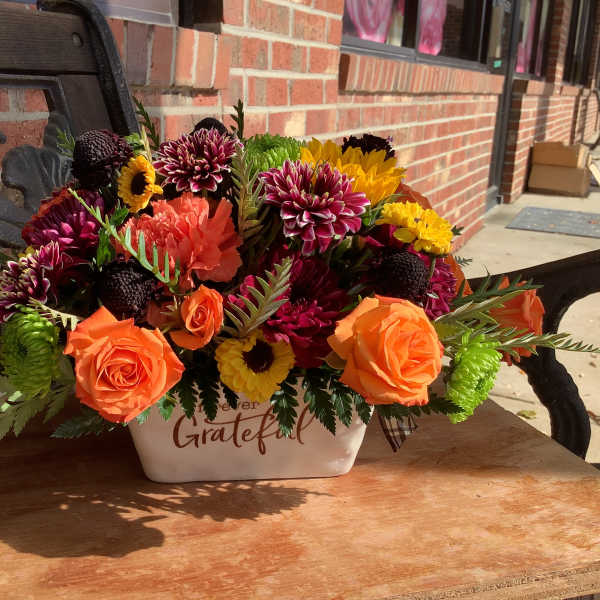 Orange roses and mixed mums in a white ceramic container