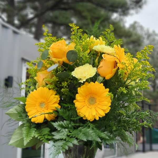 Yellow flowers and roses arranged in a clear glass vase.