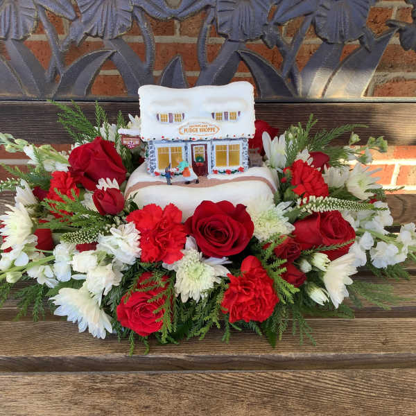 Red and white floral arrangement around a small snow-covered house decoration