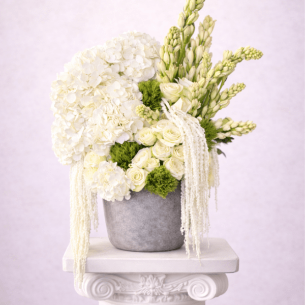 Tall white and green floral arrangement with hydrangeas and roses in a gray pot on a pedestal.
