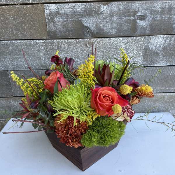 Mixed floral arrangement in a dark wooden container with roses and chrysanthemums