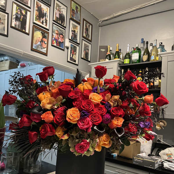 Large bouquet of red, orange, and pink roses in a black hatbox