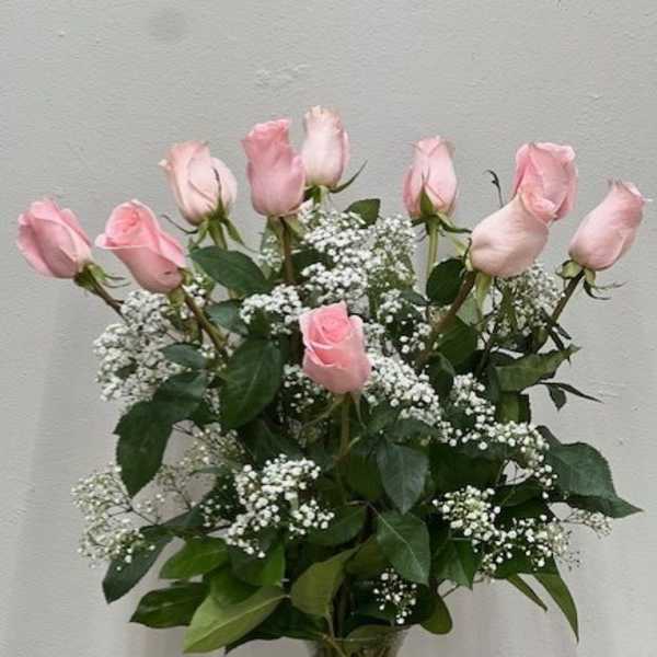Tall clear vase of light pink roses with white filler flowers arranged in a rounded display