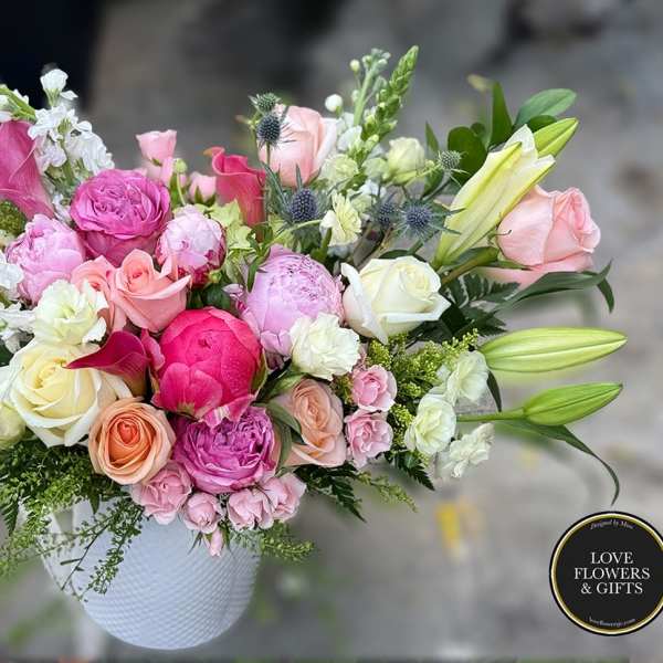 Mixed arrangement of pink peonies, roses, and lilies in a white ceramic vase