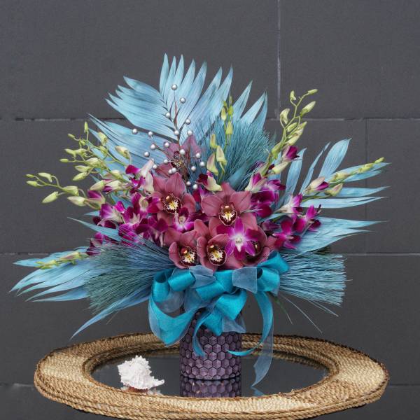 Bouquet of purple orchids and blue feathers in a decorative vase