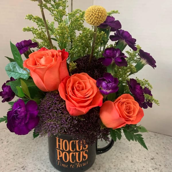 Orange roses and purple flowers arranged in a black mug