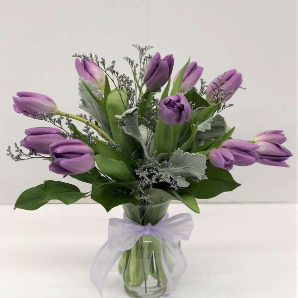 Purple tulips arranged in a glass vase with a lavender ribbon